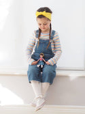 Girl playing with Lottie Doll with Dark brown hair. in white leggings and jean skirt and red/white stripe shirt