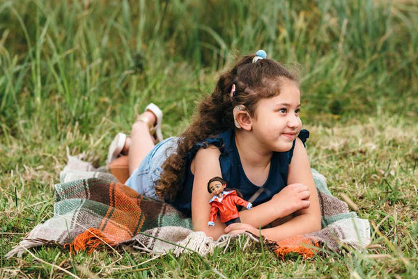 child laying on ground a blanket holding  doll