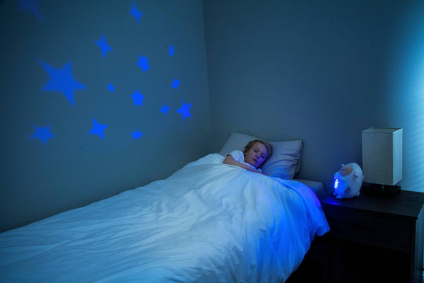 Child sleeping with White Lamb with star and moon projection lights on tummy. and the Blue stars projected on their wall
