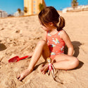 Girl in sand playing with Strawberry Blonde Lottie in Swimsuit, yellow floaties, and towel and inflatable flamingo